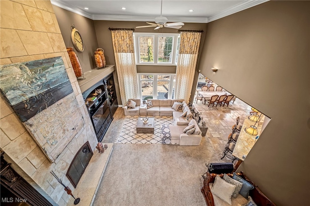 living area featuring ornamental molding, recessed lighting, a towering ceiling, a glass covered fireplace, and a ceiling fan