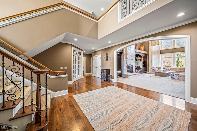 entrance foyer with wood finished floors, arched walkways, a towering ceiling, and crown molding