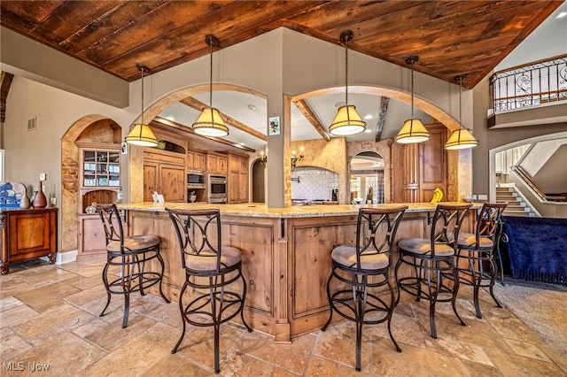 kitchen with stainless steel appliances, wood ceiling, a breakfast bar, and stone tile floors