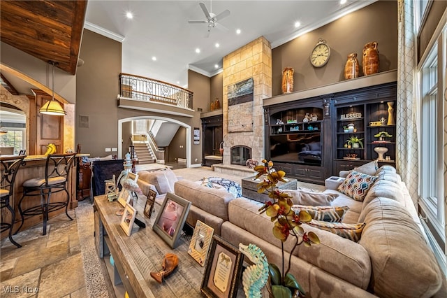 living area with crown molding, stone tile flooring, a high ceiling, arched walkways, and a ceiling fan