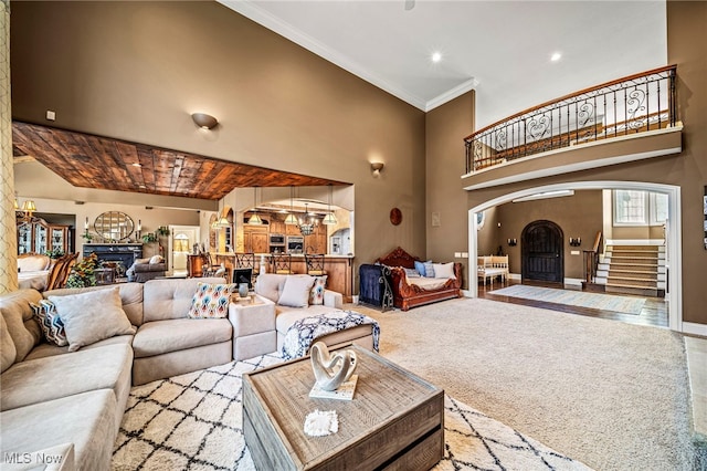 carpeted living area featuring stairway, ornamental molding, an inviting chandelier, a towering ceiling, and arched walkways