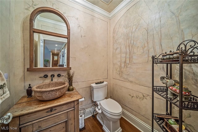 half bathroom with toilet, wood finished floors, vanity, and ornamental molding