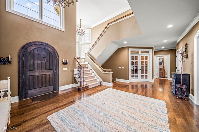 entrance foyer featuring ornamental molding, wood finished floors, arched walkways, an inviting chandelier, and baseboards