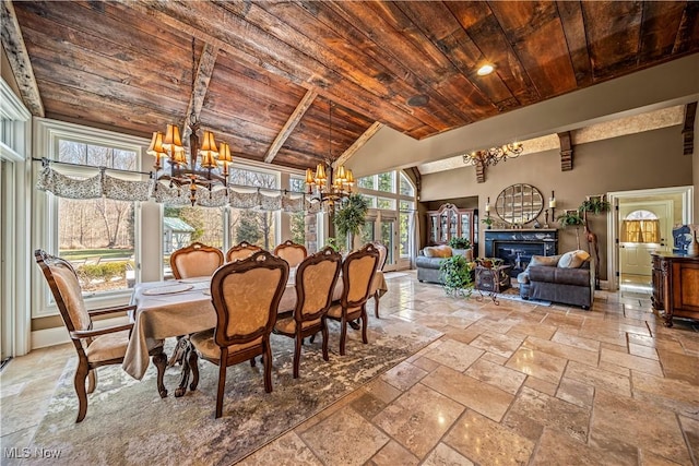 dining area with wood ceiling, vaulted ceiling, an inviting chandelier, stone tile flooring, and a glass covered fireplace