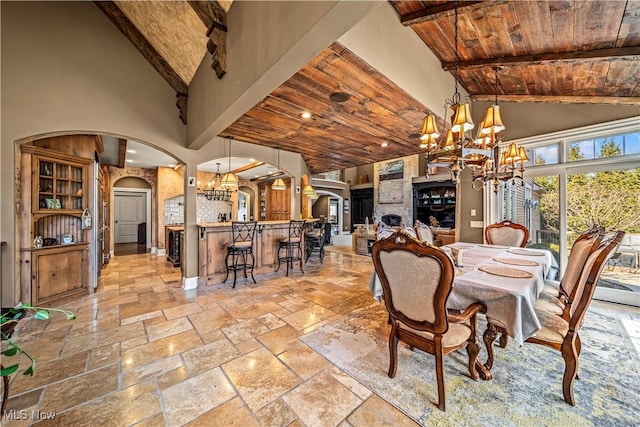 dining area with stone tile flooring, arched walkways, a notable chandelier, and wooden ceiling