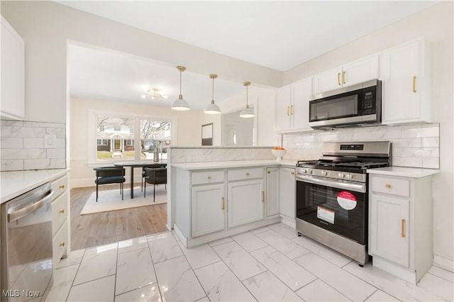 kitchen with backsplash, light countertops, a peninsula, marble finish floor, and stainless steel appliances