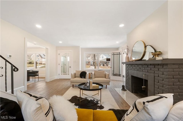 living room featuring stairway, light wood finished floors, a fireplace, and a wealth of natural light