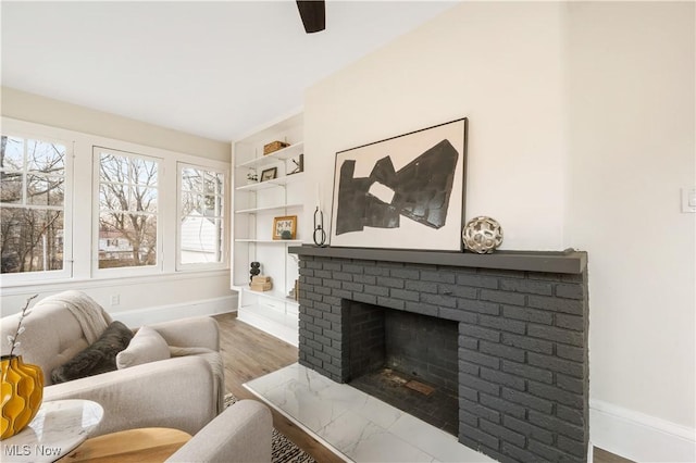 living area with built in shelves, baseboards, a fireplace, wood finished floors, and a ceiling fan