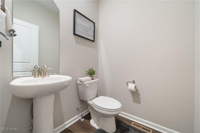 half bathroom featuring wood finished floors, baseboards, visible vents, a sink, and toilet