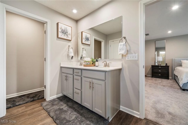 ensuite bathroom featuring wood finished floors, baseboards, and a sink