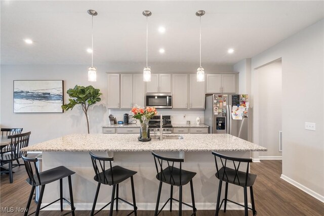 kitchen featuring a sink, stainless steel appliances, dark wood-style floors, and a center island with sink