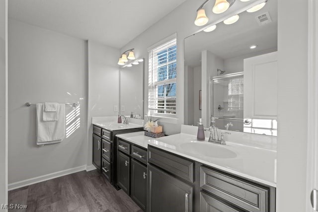 full bath with wood finished floors, visible vents, two vanities, a sink, and a shower stall