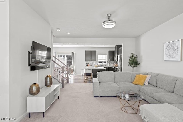 living room with stairway, baseboards, and light colored carpet