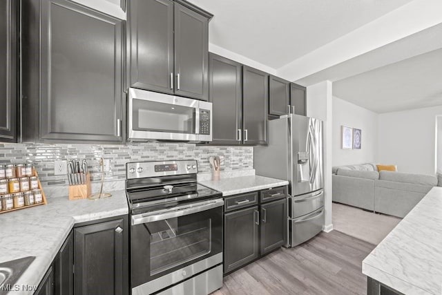 kitchen with open floor plan, backsplash, stainless steel appliances, and light wood-style floors