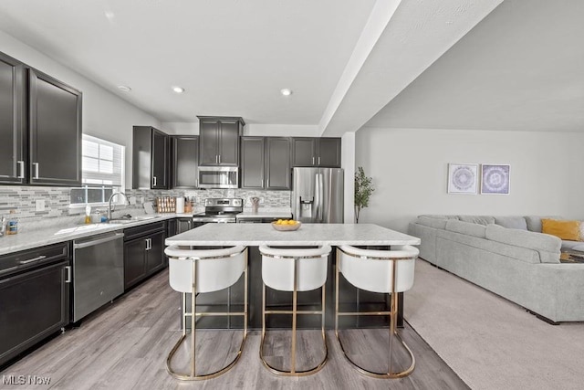 kitchen featuring backsplash, open floor plan, a kitchen bar, stainless steel appliances, and a sink