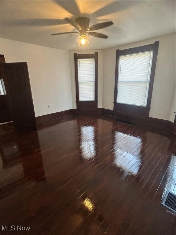 spare room with ceiling fan, visible vents, baseboards, and dark wood finished floors