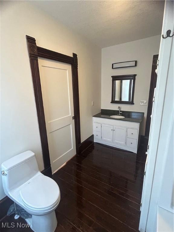 half bathroom with vanity, toilet, wood finished floors, and baseboards