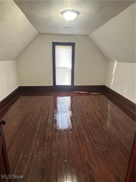 bonus room featuring vaulted ceiling, baseboards, dark wood-style flooring, and a textured ceiling