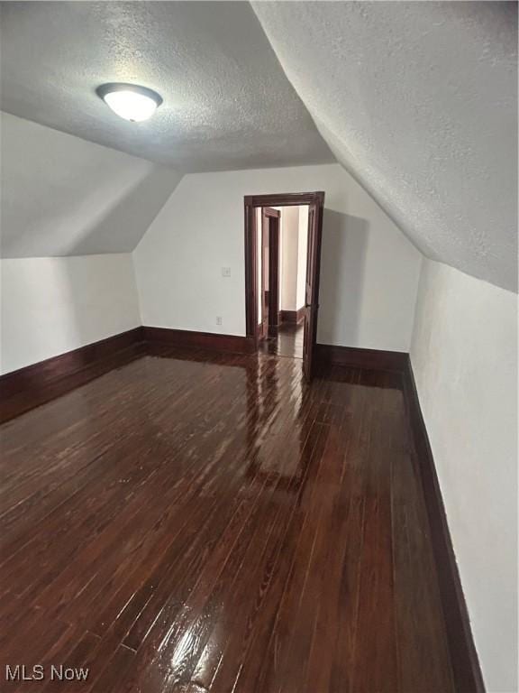 additional living space with vaulted ceiling, a textured ceiling, baseboards, and wood-type flooring