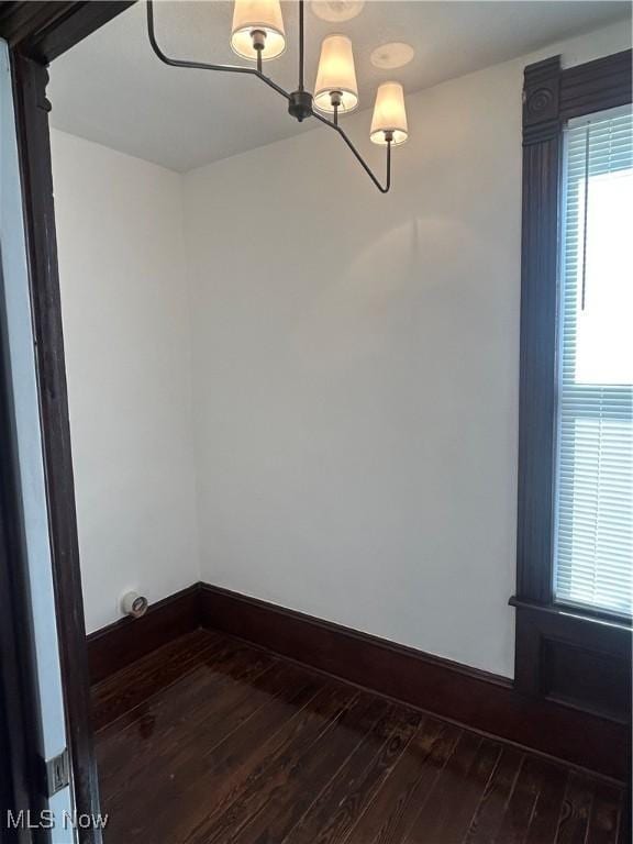 empty room featuring a notable chandelier, baseboards, and dark wood-style flooring