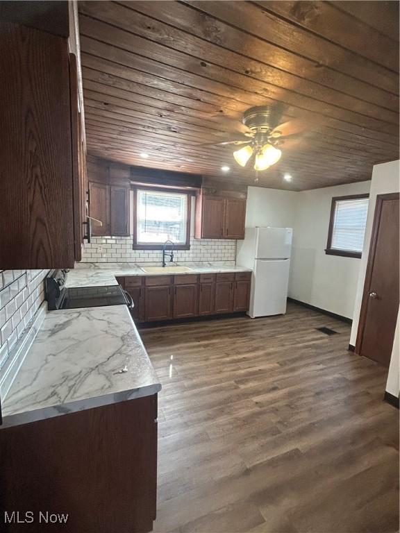 kitchen with dark wood finished floors, freestanding refrigerator, a sink, wood ceiling, and range with electric stovetop