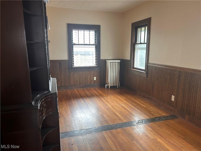 unfurnished room with hardwood / wood-style flooring, radiator heating unit, a healthy amount of sunlight, and wainscoting