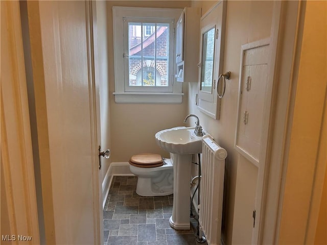 half bath with baseboards, toilet, radiator heating unit, stone finish floor, and a sink