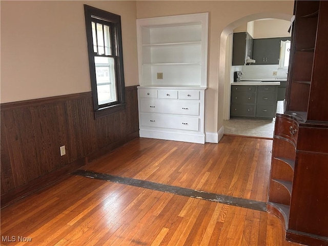 unfurnished bedroom with wooden walls, arched walkways, a wainscoted wall, and wood-type flooring