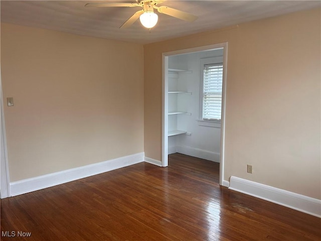 unfurnished bedroom with dark wood finished floors, a walk in closet, baseboards, and a closet