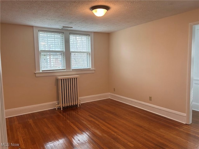 empty room with baseboards, wood-type flooring, a textured ceiling, and radiator heating unit