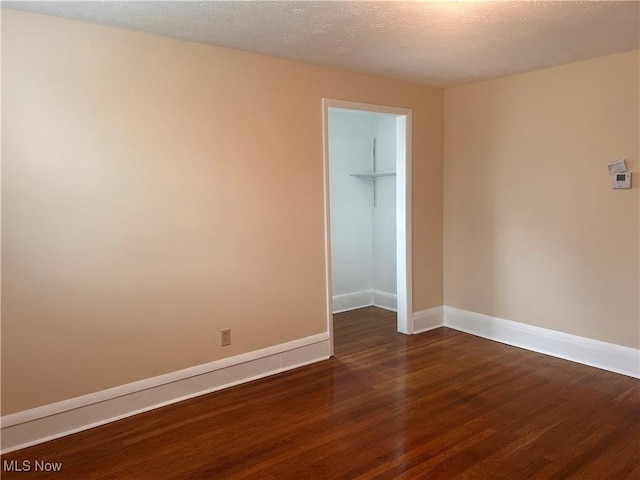 spare room featuring baseboards, dark wood-type flooring, and a textured ceiling