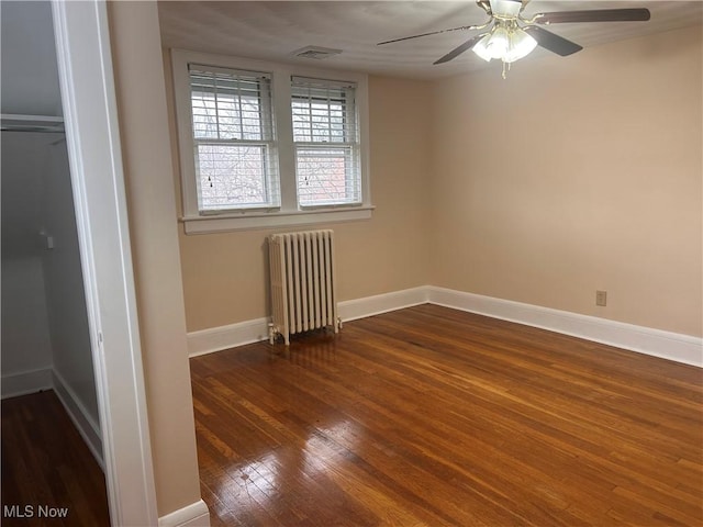 empty room with visible vents, a ceiling fan, hardwood / wood-style flooring, radiator, and baseboards