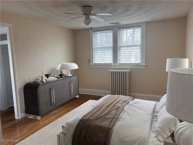 bedroom featuring visible vents, wood finished floors, radiator heating unit, baseboards, and ceiling fan