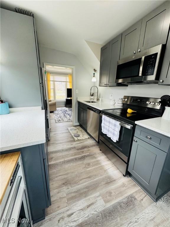 kitchen featuring light wood finished floors, stainless steel appliances, light countertops, and a sink