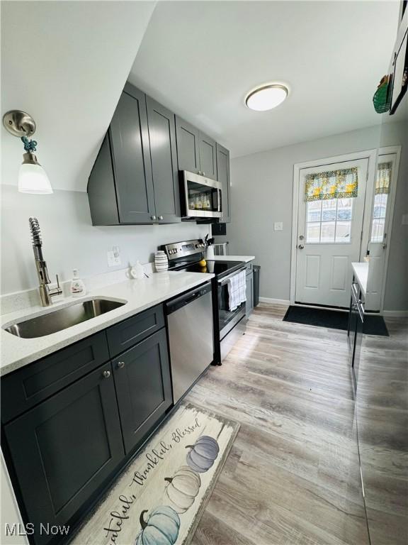 kitchen featuring light wood finished floors, appliances with stainless steel finishes, baseboards, and a sink