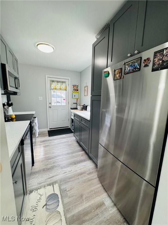 kitchen with baseboards, stainless steel appliances, light countertops, and light wood-style floors