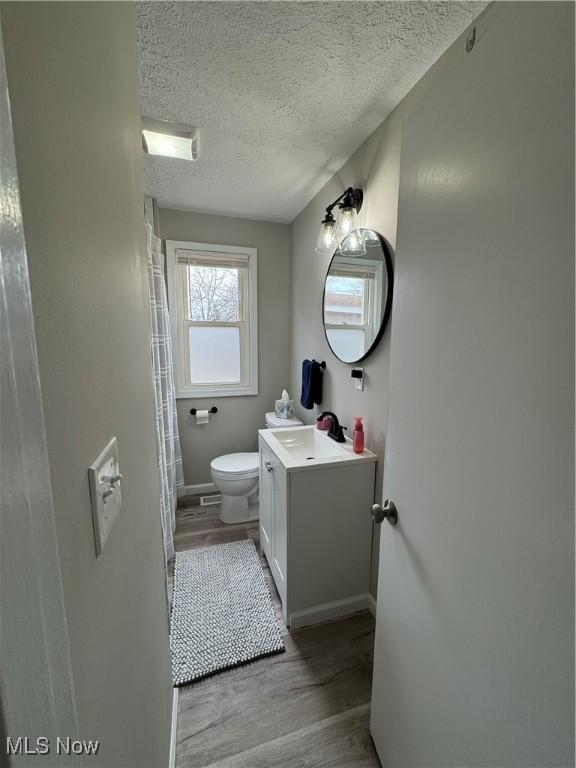 bathroom featuring vanity, wood finished floors, baseboards, a textured ceiling, and toilet