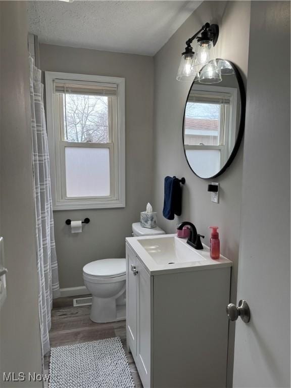 bathroom with visible vents, toilet, a textured ceiling, wood finished floors, and vanity