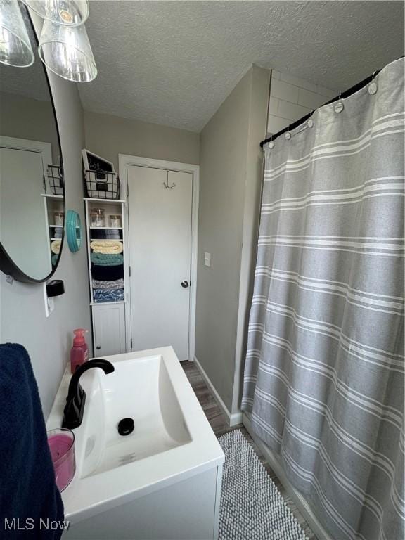 bathroom featuring a shower with shower curtain, baseboards, a textured ceiling, and vanity