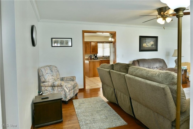 living area with dark wood-type flooring, ornamental molding, and a ceiling fan