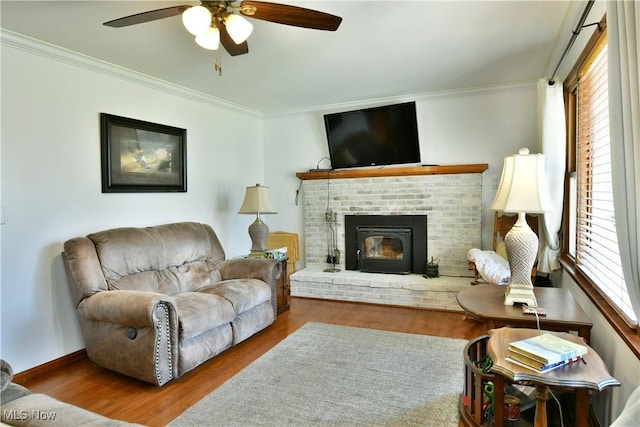 living room with ornamental molding, a ceiling fan, wood finished floors, baseboards, and a brick fireplace