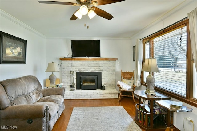 living area featuring wood finished floors, a fireplace, ornamental molding, and a ceiling fan