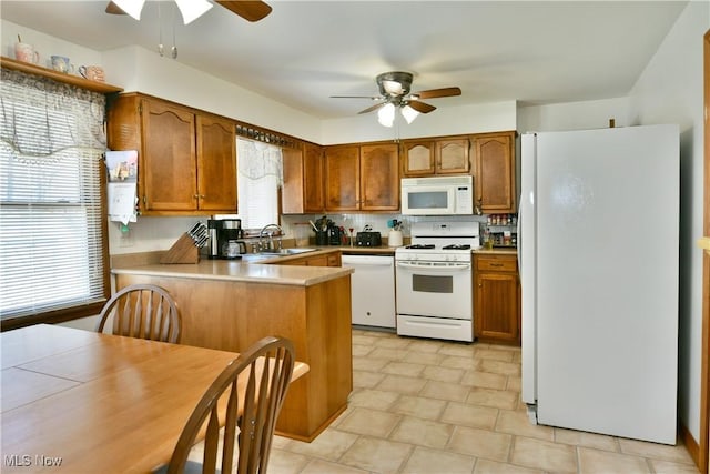 kitchen with brown cabinets, a peninsula, white appliances, a ceiling fan, and a sink