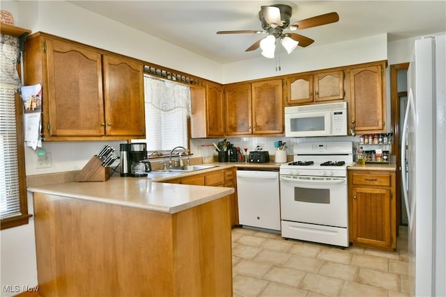 kitchen with a sink, white appliances, a peninsula, brown cabinetry, and ceiling fan