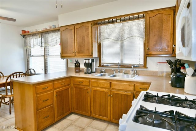 kitchen with a sink, white appliances, a peninsula, brown cabinetry, and light countertops