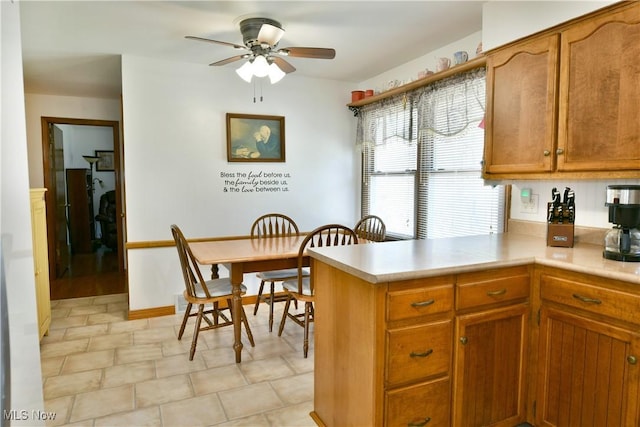 kitchen featuring a peninsula, ceiling fan, brown cabinetry, and light countertops