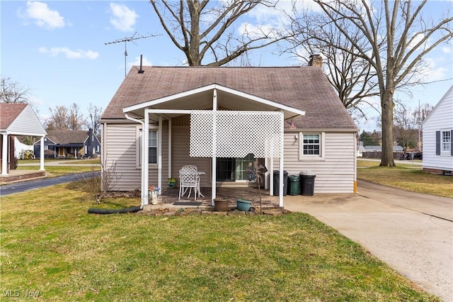 rear view of property featuring a yard, driveway, roof with shingles, and a chimney