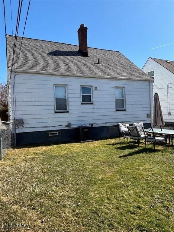 back of property featuring a yard, a shingled roof, a chimney, and fence