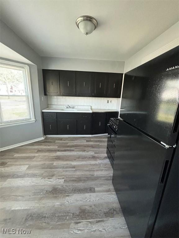 kitchen featuring dark cabinetry, black appliances, light countertops, and light wood-style floors