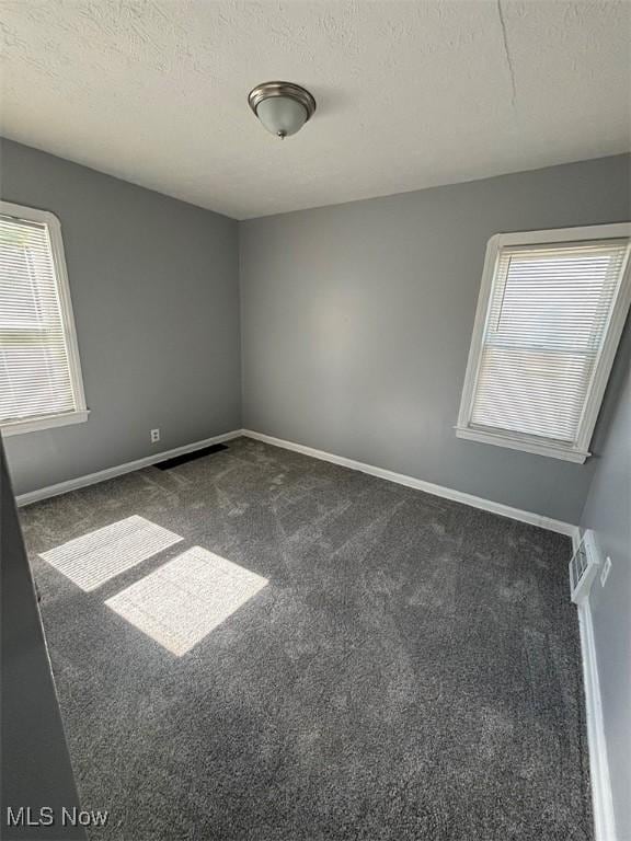 empty room with visible vents, a textured ceiling, baseboards, and dark colored carpet